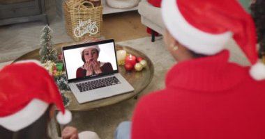 Noel Baba şapkalı çeşitli aileler, ekranda mutlu bir kadınla yılbaşı görüntüsü için laptop kullanıyorlar. Noel, şenlik ve iletişim teknolojisi.