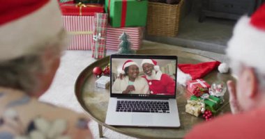 Noel Baba şapkalı son sınıf Kafkasyalı çift, ekranlarında çift olan bir çiftle yılbaşı görüntüsü için laptop kullanıyor. Noel, şenlik ve iletişim teknolojisi.