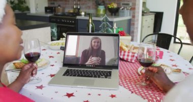 Şaraplı Afrikalı Amerikalı çift, ekranda mutlu bir kadınla yılbaşı görüntüsü için dizüstü bilgisayar kullanıyor. Noel, şenlik ve iletişim teknolojisi.