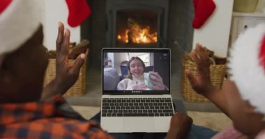 Noel Baba şapkalı Afro-Amerikan çift, ekranda kadınla birlikte dizüstü bilgisayar kullanıyor. Noel, şenlik ve iletişim teknolojisi.