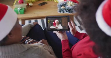 Afrika kökenli Amerikalı anne ve kız. Ekranda bir kadınla Noel videosu için tablet kullanıyorlar. Noel, şenlik ve iletişim teknolojisi.
