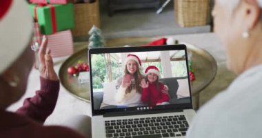 Farklı son sınıf kız arkadaşları, ekranda mutlu bir aileyle yılbaşı videosu için dizüstü bilgisayar kullanıyor. Noel, şenlik ve iletişim teknolojisi.