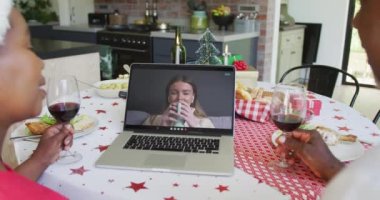 Şaraplı Afrikalı Amerikalı çift, ekranda mutlu bir kadınla yılbaşı görüntüsü için dizüstü bilgisayar kullanıyor. Noel, şenlik ve iletişim teknolojisi.