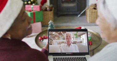 Farklı son sınıf kız arkadaşları, ekranda mutlu bir kadınla yılbaşı görüntüsü için dizüstü bilgisayar kullanıyor. Noel, şenlik ve iletişim teknolojisi.