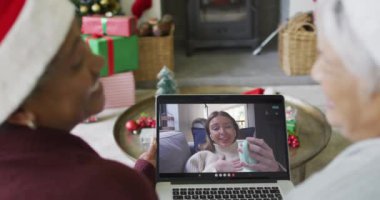 Farklı son sınıf kız arkadaşları, ekranda mutlu bir kadınla yılbaşı görüntüsü için dizüstü bilgisayar kullanıyor. Noel, şenlik ve iletişim teknolojisi.