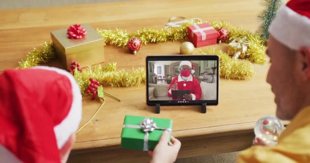 サンタの帽子をかぶった白人の父親と息子は 画面上のサンタとクリスマスビデオコールのタブレットを使用しています 19大流行期のクリスマスやお祭りや通信技術は — ストック動画