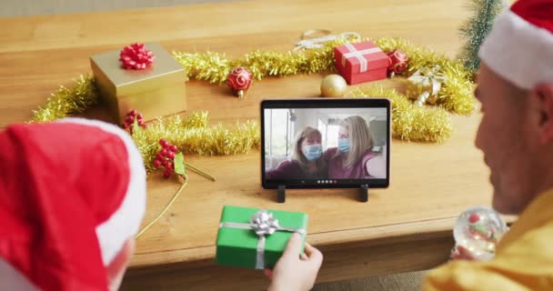 スクリーン上の家族とクリスマスビデオコールのタブレットを使用してサンタの帽子を持つ白人の父と息子 19大流行期のクリスマスやお祭りや通信技術は — ストック動画