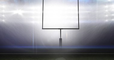 Gece vakti aydınlatılmış parlak Amerikan futbol stadyumuna karşı boş kale direği. Spor sahasında parlayan ışıklar ve mercek parlaması.