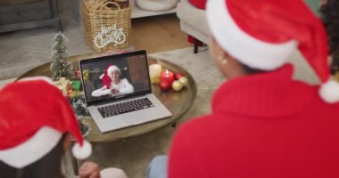 Noel Baba şapkalı çeşitli aileler, ekranda mutlu bir kadınla yılbaşı görüntüsü için laptop kullanıyorlar. Noel, şenlik ve iletişim teknolojisi.