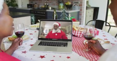 Şaraplı Afrika kökenli Amerikalı bir çift Noel 'de ekranda mutlu bir Noel Baba' yla dizüstü bilgisayar kullanıyor. Noel, şenlik ve iletişim teknolojisi.