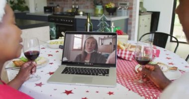 Şaraplı Afrikalı Amerikalı çift, ekranda mutlu bir kadınla yılbaşı görüntüsü için dizüstü bilgisayar kullanıyor. Noel, şenlik ve iletişim teknolojisi.