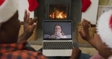 Noel Baba şapkalı Afro-Amerikan çift, ekranda kadınla birlikte dizüstü bilgisayar kullanıyor. Noel, şenlik ve iletişim teknolojisi.