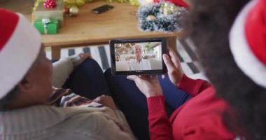 Afrika kökenli Amerikalı anne ve kız. Ekranda bir kadınla Noel videosu için tablet kullanıyorlar. Noel, şenlik ve iletişim teknolojisi.