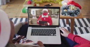Afrika kökenli Amerikalı anne ve kız Noel 'de ekranda Noel Baba' nın görüntülü araması için laptop kullanıyorlar. Covid 19 salgını sırasında Noel, şenlik ve iletişim teknolojisi.
