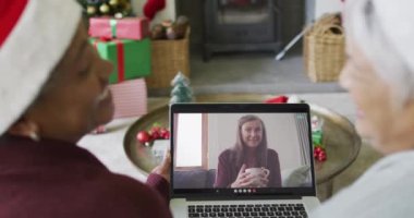Farklı son sınıf kız arkadaşları, ekranda mutlu bir kadınla yılbaşı görüntüsü için dizüstü bilgisayar kullanıyor. Noel, şenlik ve iletişim teknolojisi.