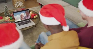 Noel Baba şapkalı çeşitli aileler, ekranda mutlu çiftle Noel görüntülü konuşma yapmak için laptop kullanıyorlar. Noel, şenlik ve iletişim teknolojisi.