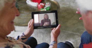 Kafkasyalı üst düzey bir çift, ekranda mutlu bir kadınla Noel videosu için tablet kullanıyor. Noel, şenlik ve iletişim teknolojisi.