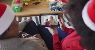 Afrika kökenli Amerikalı anne ve kız. Ekranda aileleriyle birlikte yılbaşı videosu için tablet kullanıyorlar. Noel, şenlik ve iletişim teknolojisi.