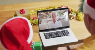 Noel Baba şapkalı beyaz bir baba ve oğul, ekranda bir kadınla yılbaşı görüntüsü için dizüstü bilgisayar kullanıyorlar. Noel, şenlik ve iletişim teknolojisi.