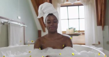 Mutlu Afro-Amerikan kadının üzerine düşen altın konfetilerin animasyonu evde banyoda dinleniyor. Rahatlama, sağlık ve refah kutlaması konsepti dijital olarak oluşturulmuş video.