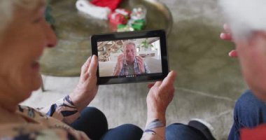 Beyaz üst düzey bir çift gülümsüyor ve ekranda bir adamla noel videosu için tablet kullanıyorlar. Noel, şenlik ve iletişim teknolojisi.