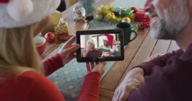 Noel Baba şapkalı beyaz bir çift Noel 'de ekranda aileleriyle birlikte tablet kullanıyor. Noel, şenlik ve iletişim teknolojisi.