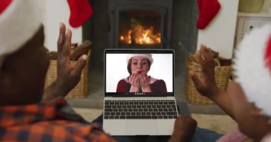 Noel Baba şapkalı Afro-Amerikan çift, ekranda kadınla birlikte dizüstü bilgisayar kullanıyor. Noel, şenlik ve iletişim teknolojisi.