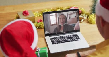 Noel Baba şapkalı beyaz bir baba ve oğul, ekranda bir kadınla yılbaşı görüntüsü için dizüstü bilgisayar kullanıyorlar. Noel, şenlik ve iletişim teknolojisi.