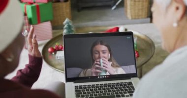 Farklı son sınıf kız arkadaşları, ekranda mutlu bir kadınla yılbaşı görüntüsü için dizüstü bilgisayar kullanıyor. Noel, şenlik ve iletişim teknolojisi.