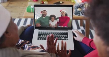 Afrika kökenli Amerikalı anne ve kız, ekranda ailesiyle birlikte yılbaşı görüntülü konuşma için dizüstü bilgisayar kullanıyorlar. Noel, şenlik ve iletişim teknolojisi.