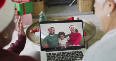 Farklı son sınıf kız arkadaşları, ekranda mutlu bir aileyle yılbaşı videosu için dizüstü bilgisayar kullanıyor. Noel, şenlik ve iletişim teknolojisi.