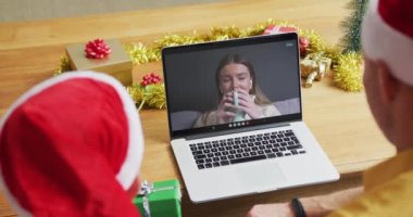 Noel Baba şapkalı beyaz bir baba ve oğul, ekranda bir kadınla yılbaşı görüntüsü için dizüstü bilgisayar kullanıyorlar. Noel, şenlik ve iletişim teknolojisi.