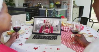 Şaraplı Afrikalı Amerikalı çift, ekranda mutlu bir kadınla yılbaşı görüntüsü için dizüstü bilgisayar kullanıyor. Noel, şenlik ve iletişim teknolojisi.