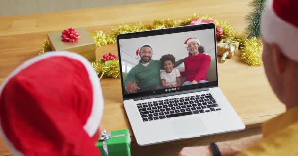 スクリーン上の家族とクリスマスのビデオ通話のためのラップトップを使用してサンタの帽子を持つ白人の父と息子 クリスマスやお祭りや通信技術は — ストック動画