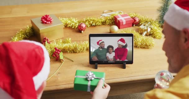 スクリーン上の家族とクリスマスビデオコールのタブレットを使用してサンタの帽子を持つ白人の父と息子 クリスマスやお祭りや通信技術は — ストック動画