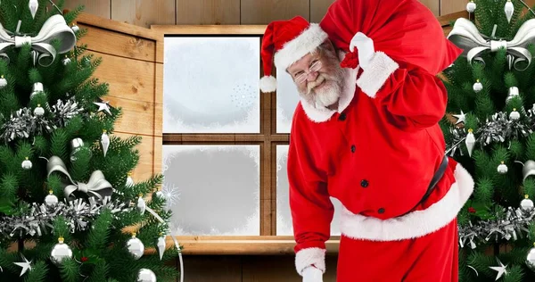 Složení Santa Clause Nesoucího Dárkový Pytel Vánočních Stromků Proti Oknu — Stock fotografie