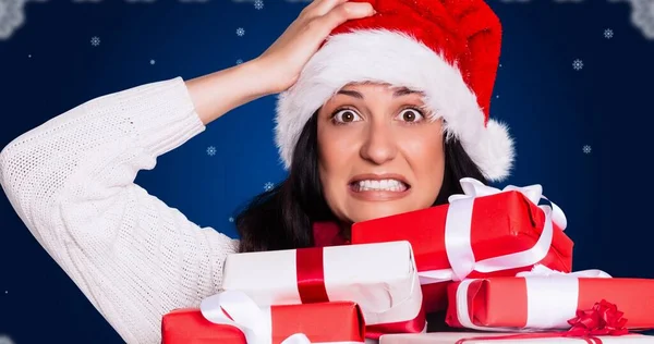 青い背景の上にクリスマスプレゼントのスタックとサンタの帽子の心配若い女性の肖像画 クリスマスのお祭り伝統と冬の休日 — ストック写真