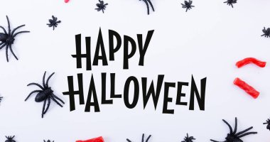 Beyaz masadaki ürkütücü örümcek süslemeleri arasında geçen mutlu Cadılar Bayramı metninin dijital kompozit görüntüsü. kültür, kutlama ve korku.