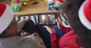 Afrika kökenli Amerikalı anne ve kız. Ekranda bir kadınla Noel videosu için tablet kullanıyorlar. Noel, şenlik ve iletişim teknolojisi.