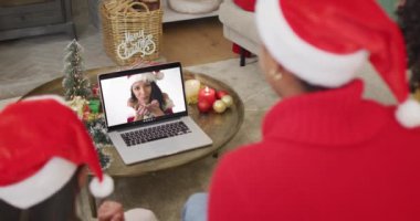 Noel Baba şapkalı çeşitli aileler, ekranda mutlu bir kadınla yılbaşı görüntüsü için laptop kullanıyorlar. Noel, şenlik ve iletişim teknolojisi.