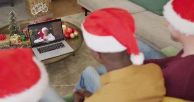 Noel Baba şapkalı çeşitli aileler, ekranda mutlu bir kadınla yılbaşı görüntüsü için laptop kullanıyorlar. Noel, şenlik ve iletişim teknolojisi.