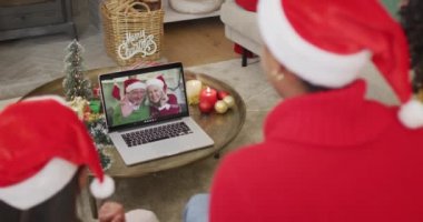 Noel Baba şapkalı çeşitli aileler, ekranda mutlu çiftle Noel görüntülü konuşma yapmak için laptop kullanıyorlar. Noel, şenlik ve iletişim teknolojisi.