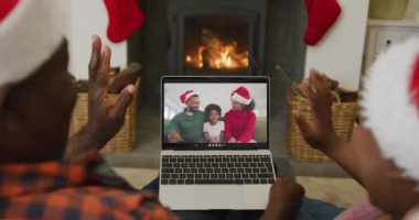 Noel Baba şapkalı Afro-Amerikalı çift, ekranda aileleriyle yılbaşı görüntüsü için dizüstü bilgisayar kullanıyor. Noel, şenlik ve iletişim teknolojisi.
