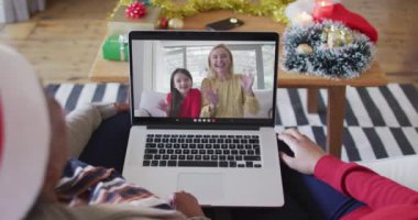 Afrika kökenli Amerikalı anne ve kız, ekranda ailesiyle birlikte yılbaşı görüntülü konuşma için dizüstü bilgisayar kullanıyorlar. Noel, şenlik ve iletişim teknolojisi.