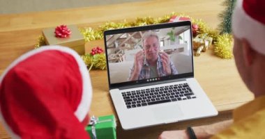 Noel Baba şapkalı beyaz bir baba ve oğul, ekrandaki adamla yılbaşı görüntülerinde dizüstü bilgisayar kullanıyorlar. Noel, şenlik ve iletişim teknolojisi.