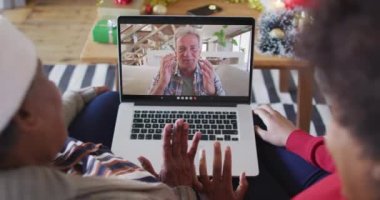 Afrika kökenli Amerikalı anne ve kız. Ekrandaki adamla yılbaşı videosu için dizüstü bilgisayar kullanıyorlar. Noel, şenlik ve iletişim teknolojisi.