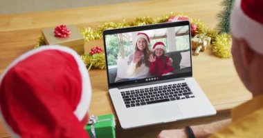 Noel Baba şapkalı beyaz bir baba ve oğul, ekranda aileleriyle yılbaşı görüntülerinde dizüstü bilgisayar kullanıyorlar. Noel, şenlik ve iletişim teknolojisi.