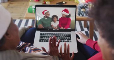 Afrika kökenli Amerikalı anne ve kız, ekranda ailesiyle birlikte yılbaşı görüntülü konuşma için dizüstü bilgisayar kullanıyorlar. Noel, şenlik ve iletişim teknolojisi.