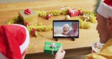 Noel Baba şapkalı beyaz bir baba ve oğul. Ekranda bir çiftin Noel görüntülü konuşması için tablet kullanıyorlar. Noel, şenlik ve iletişim teknolojisi.