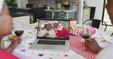 Şaraplı Afro-Amerikalı çift, mutlu çiftle Noel görüntülü konuşma yapmak için dizüstü bilgisayar kullanıyor. Noel, şenlik ve iletişim teknolojisi.